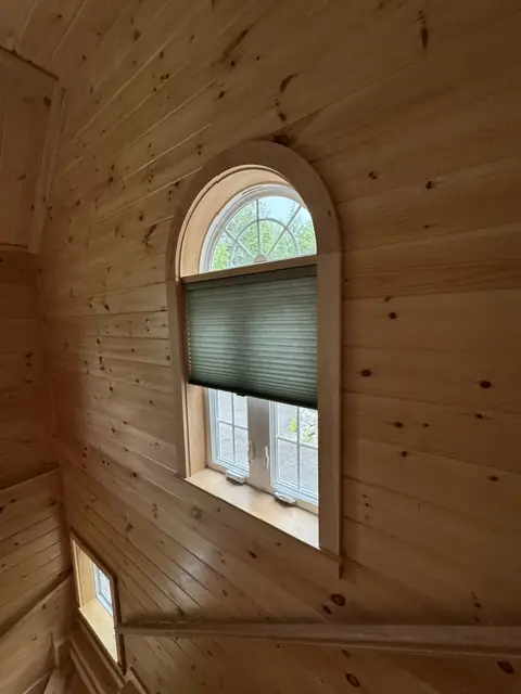 Cellular shade fitted to an arched window in a knotty-pine wall