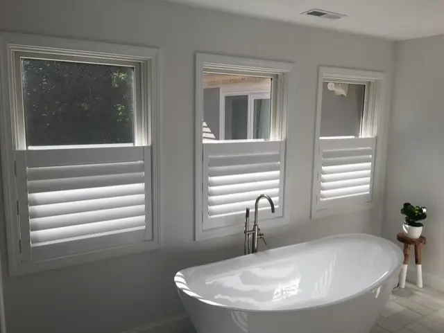 Café-style shutters on three bathroom windows above a freestanding tub