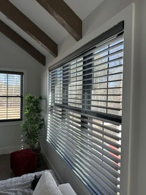 Dark-vaned sheer shadings across a wide window under exposed ceiling beams