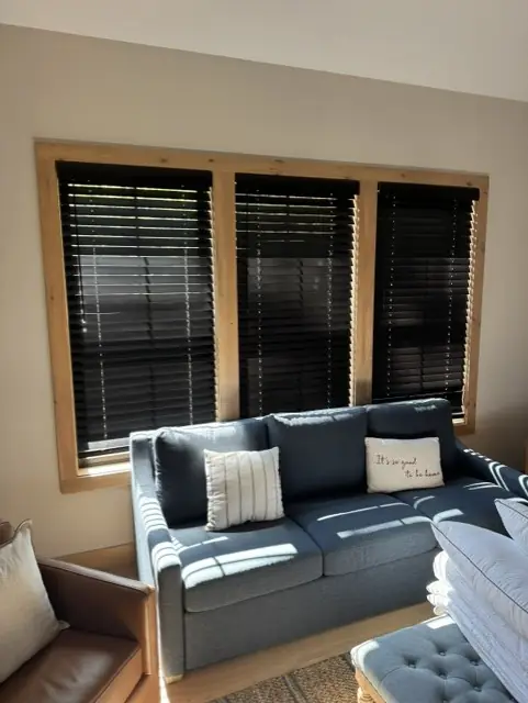 Dark wood blinds on three windows above a grey sofa