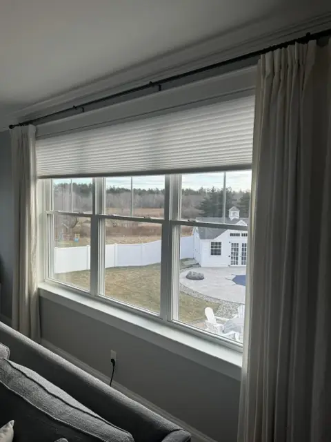 Cellular shade layered under grey drapery panels in a living room
