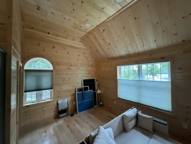 Cellular shades on an arched window and a picture window in a knotty-pine room