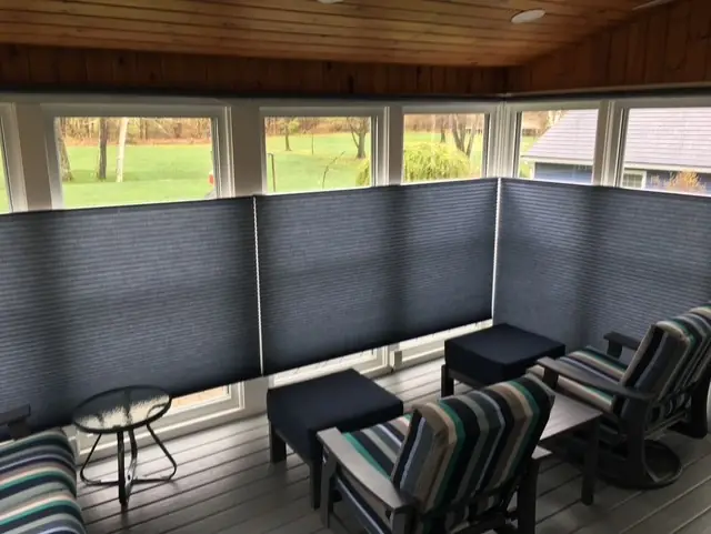Dark cellular shades lowered around a screened porch with striped armchairs