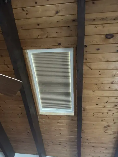 Cellular shade fitted inside a skylight in a pine ceiling with dark beams